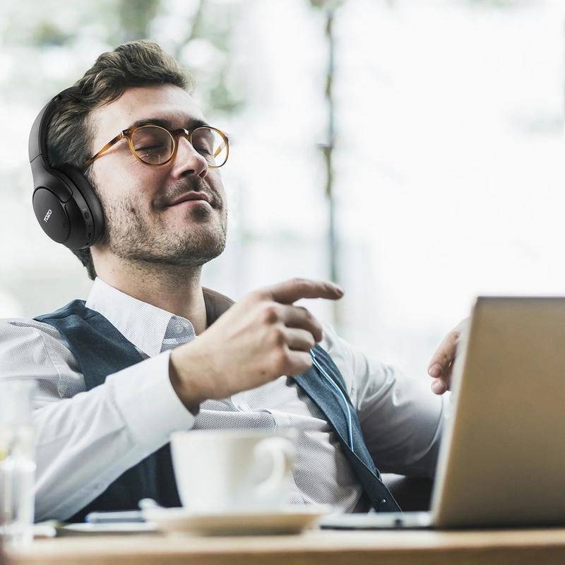 Man enjoying music with TOZO HT2 ANC Headphones while working on a laptop in a cafe.