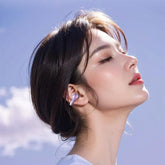 Model wearing open ear wireless earbuds against a blue sky, showcasing sports design and stylish look.
